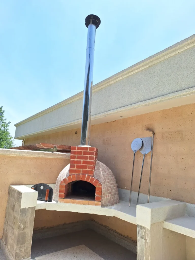 Outdoor brick pizza oven with chimney and pizza peels, built by Kenbrick Ovens