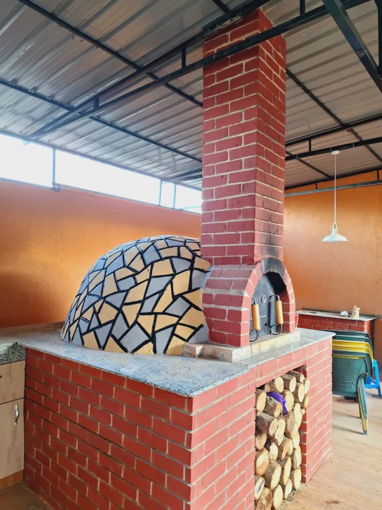 Mosaic-tiled dome pizza oven with red brick chimney and firewood store